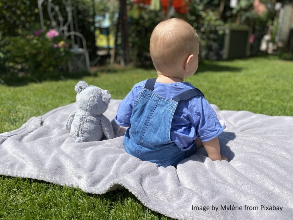 Baby sitzt auf Spieldecke im Garten