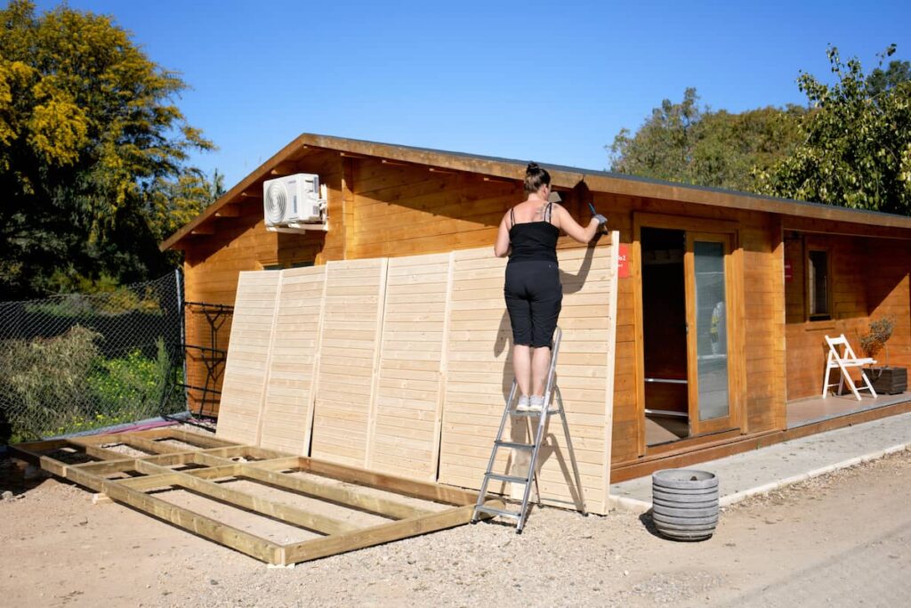 Sauna-Holzunterbau und -Wände, noch nicht zusammengebaut; Frau beim Auftragen von Holzschutzmittel
